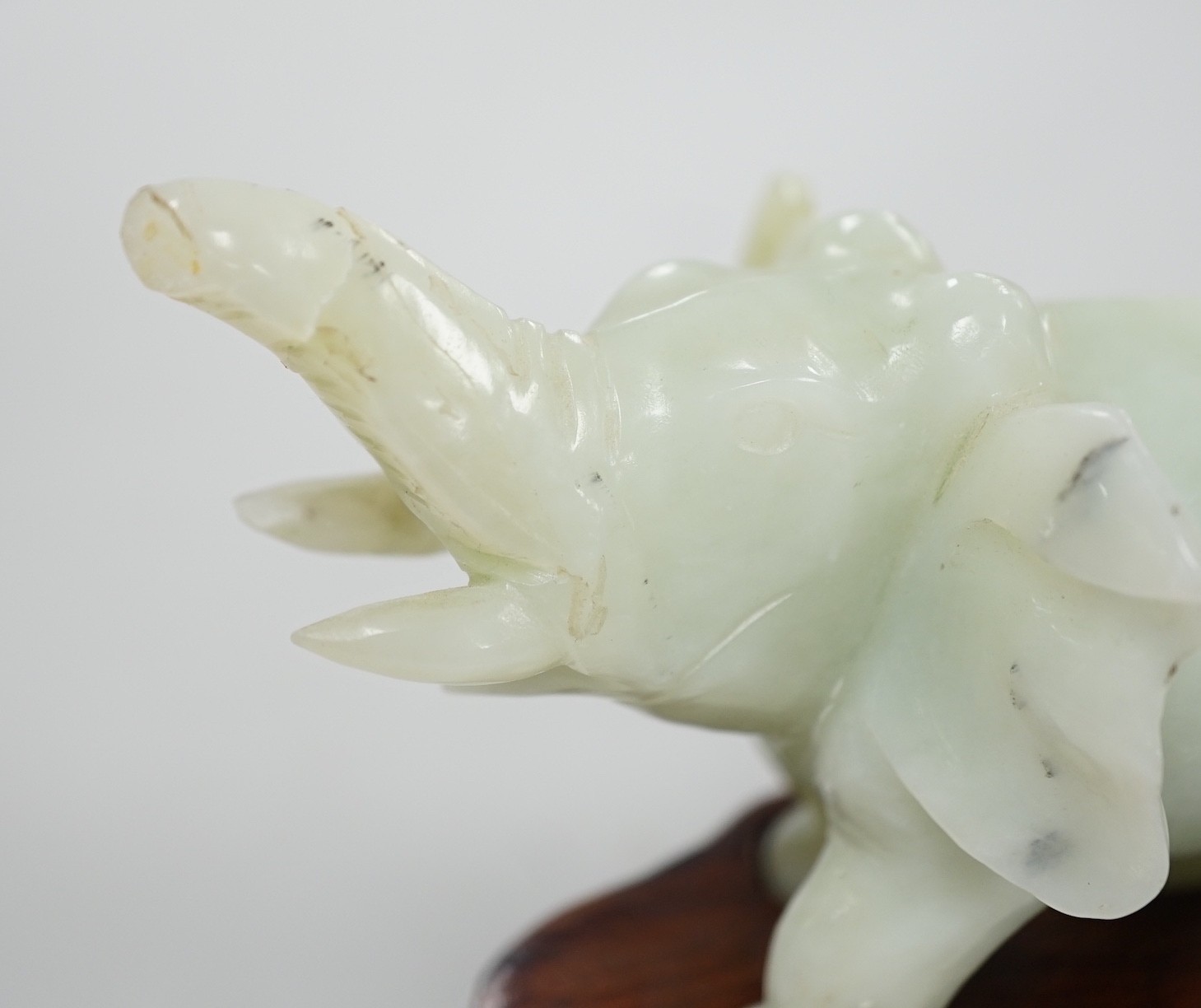 A Chinese bowenite jade elephant on hard wood stand, 11cm tall